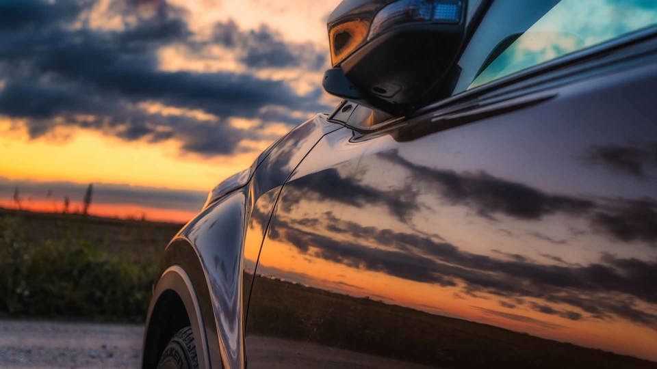 Side of black car with a sunset reflecting on it