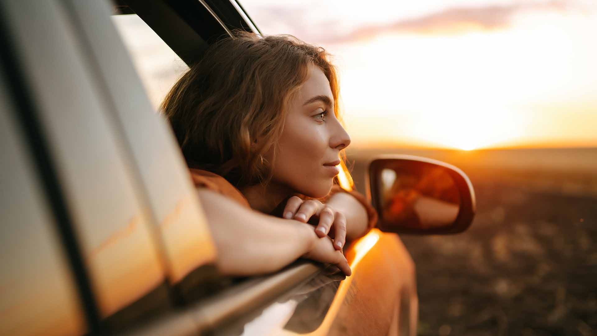 Woman with her head out of a window looking at a sunset