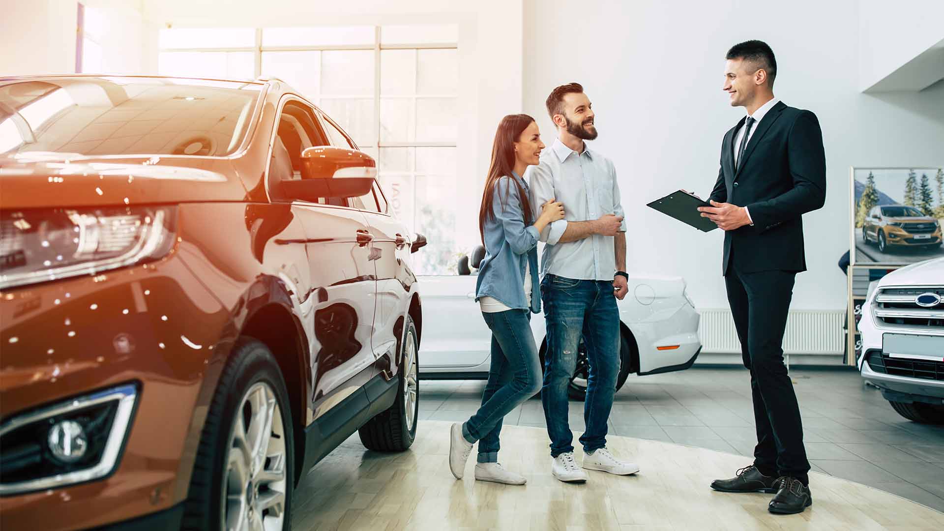 Couple stood next to orange car and talking to a salesperson