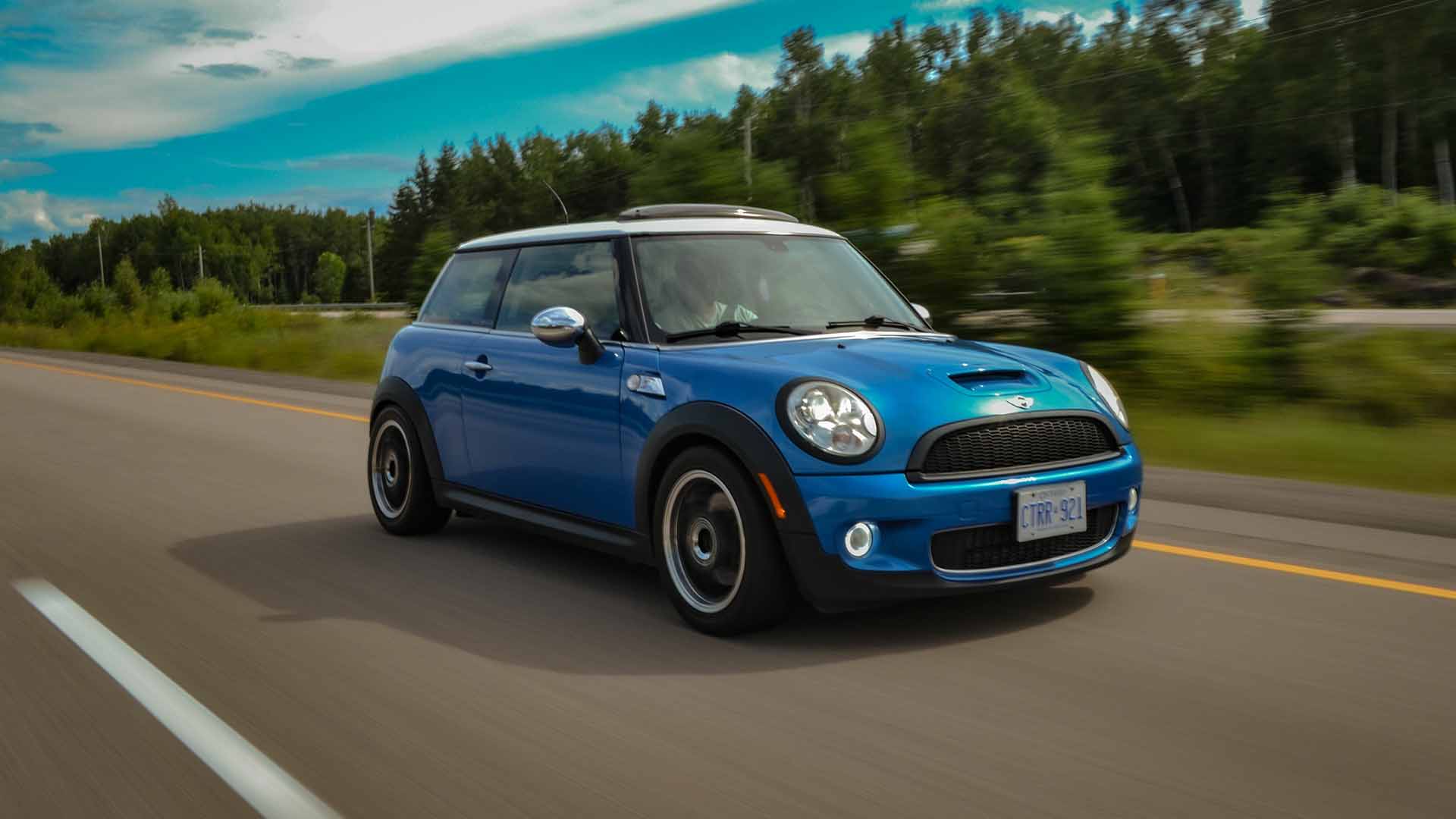 Blue Mini driving fast past trees