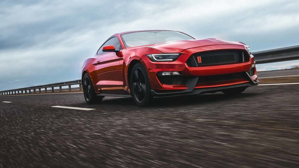 Red Ford Mustang driving along an empty road